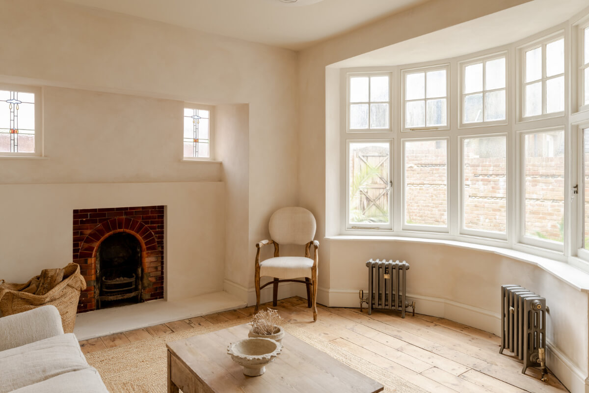 A Light Rustic Farmhouse-Style in an English Cottage 5 brick fireplace and bay window in serene living room with wooden floor and plaster walls nordroom