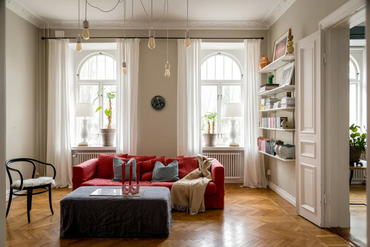Large Rooms in an Art Nouveau Apartment in Sweden 2 living room with arched windows parquet floor and red sofa